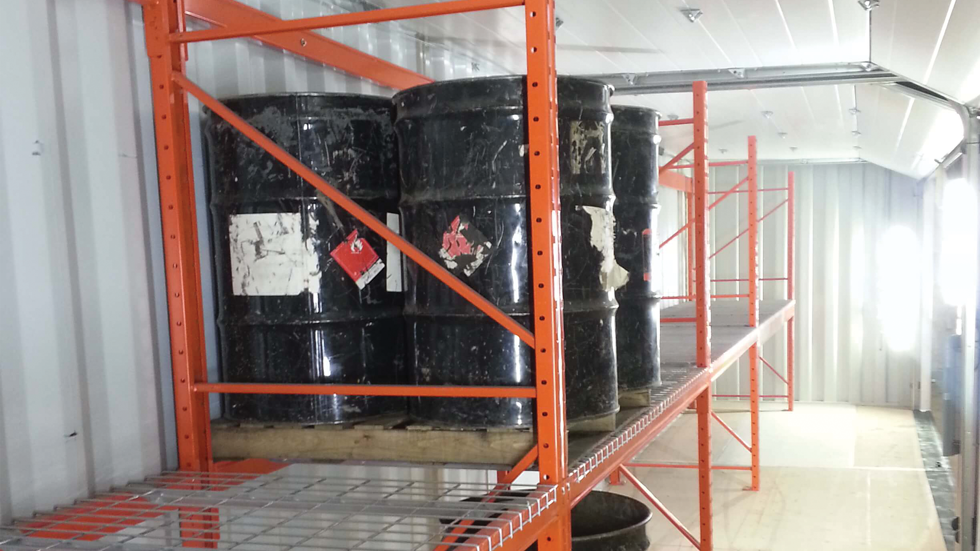 Black oil barrels sitting on orange shelf inside of container