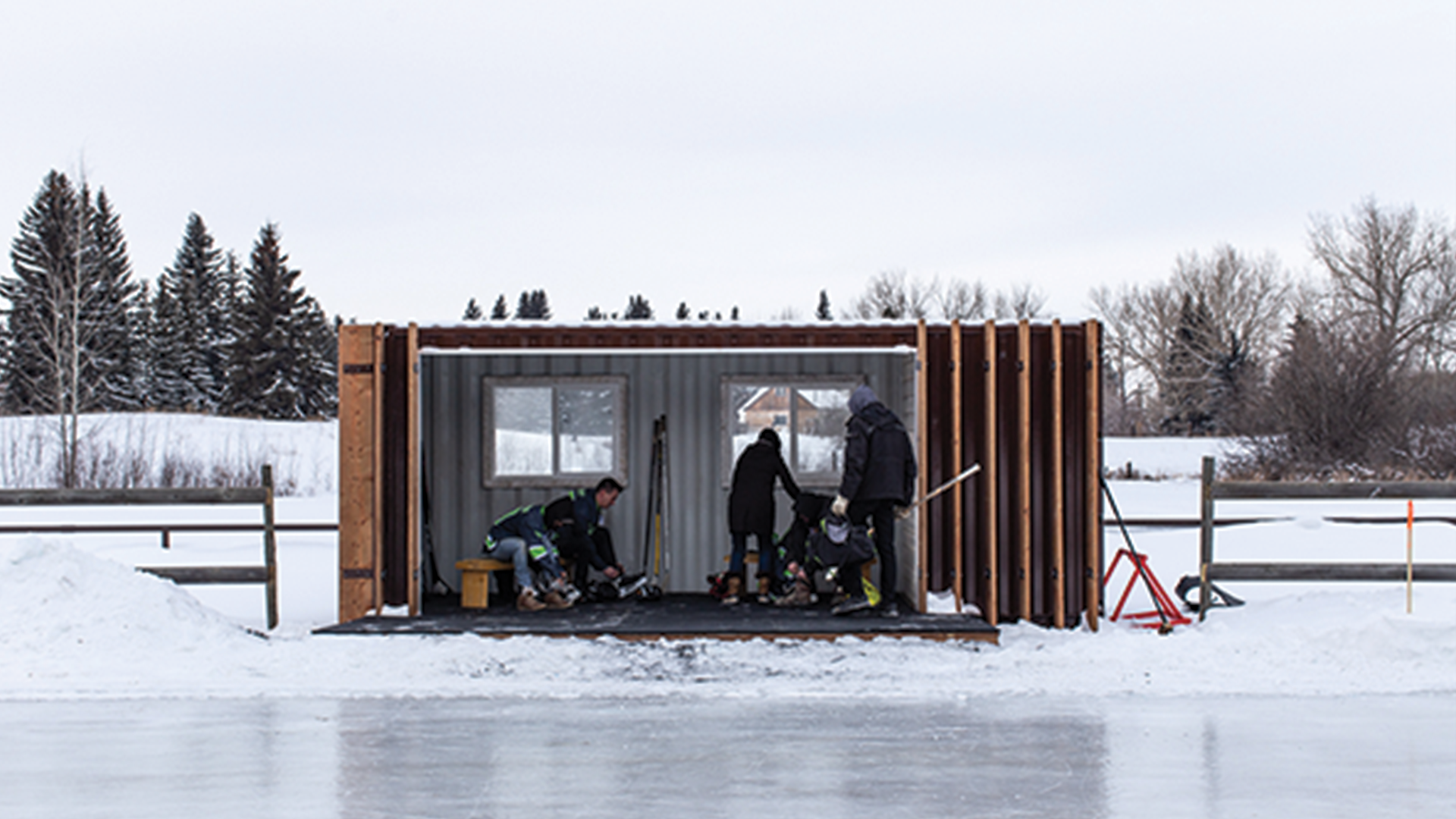 Group of people tying skates inside of container beside a skating rink