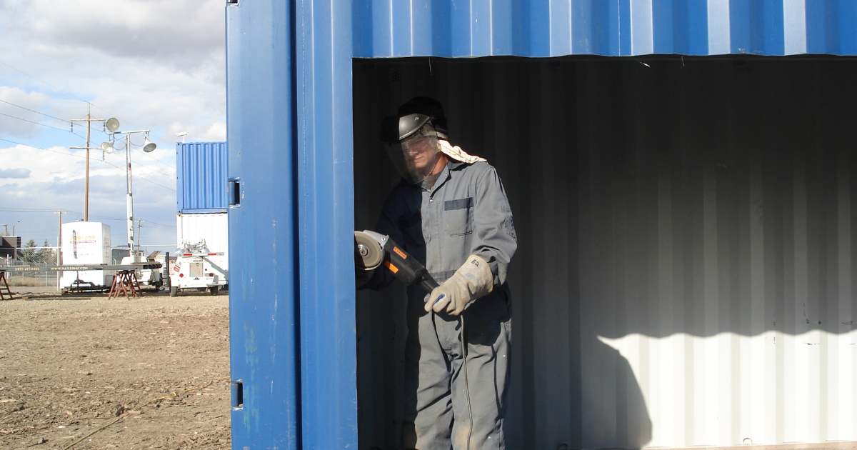 Male in safety equipment grinding the inside of a cut out piece of a container