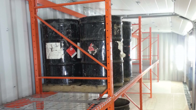 Black oil barrels on top of orange shelf inside of container