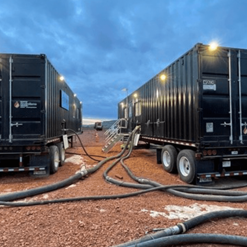 Two black containers on truck trailers with cables connected to both